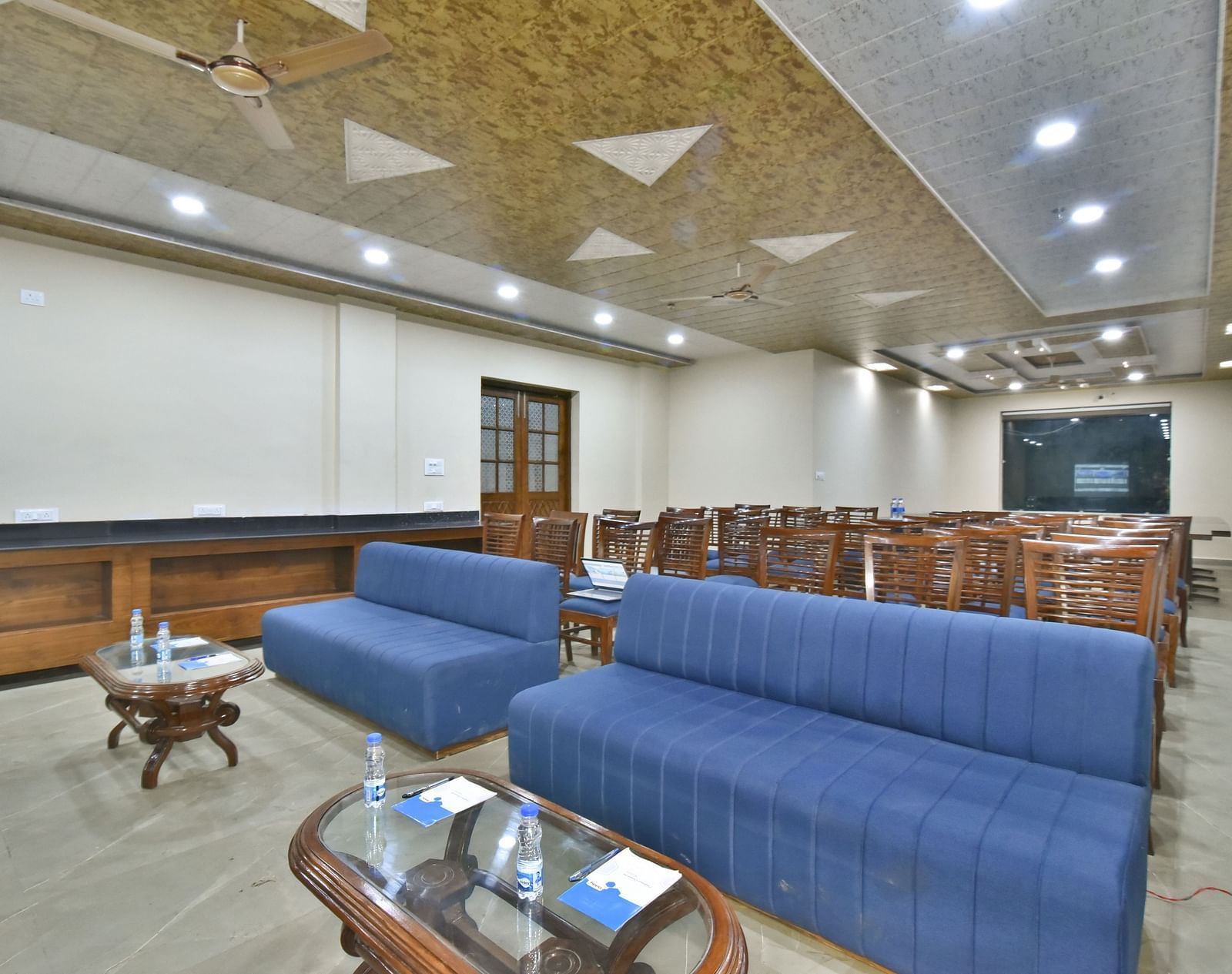 A banquet hall with a blue sofa and wooden chairs facing the podium at DLS Ark Holiday Inn, Banikhet.