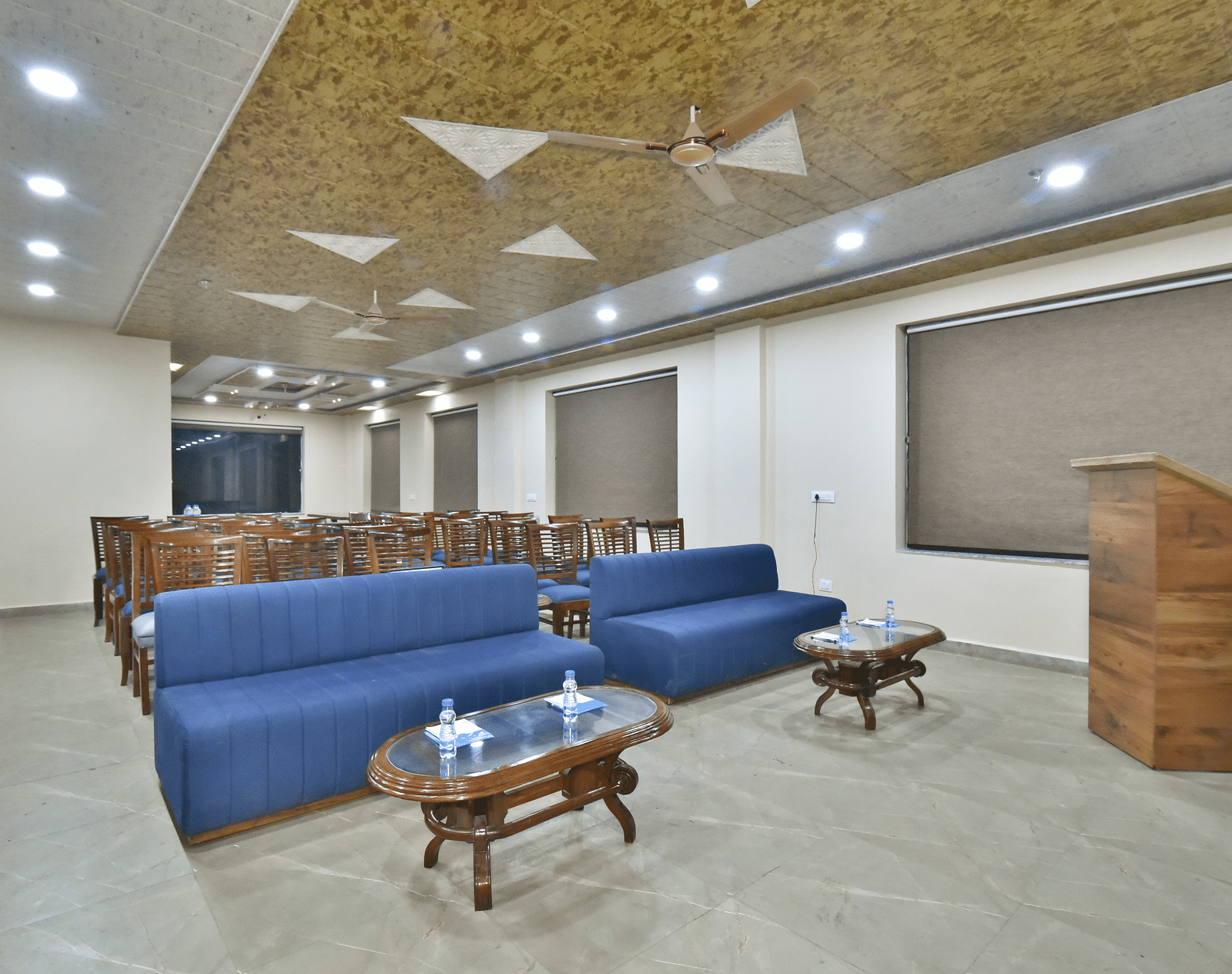 A banquet hall with a blue sofa and wooden chairs facing the podium at DLS Ark Holiday Inn, Banikhet.