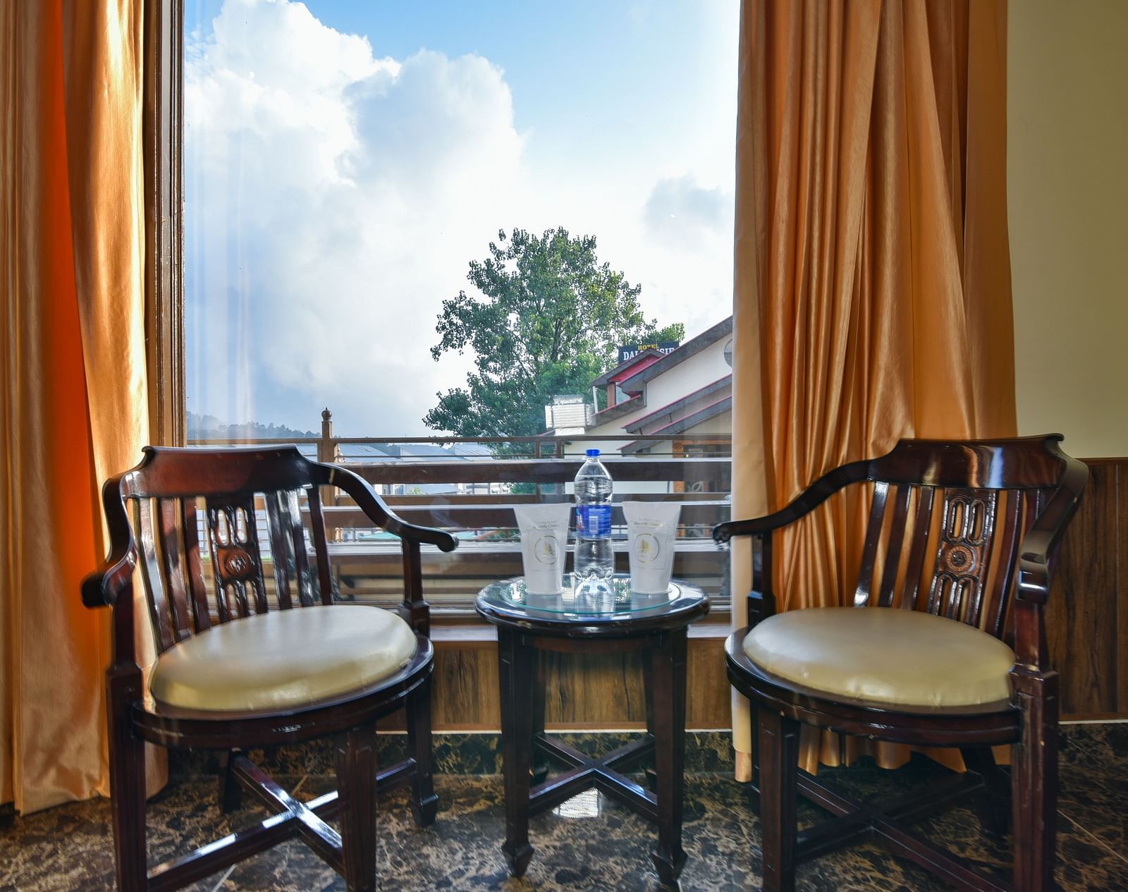 Sitting area of a Deluxe Room at DLS Dalhousie Valley Resort with brow chairs, a large window and a table.
