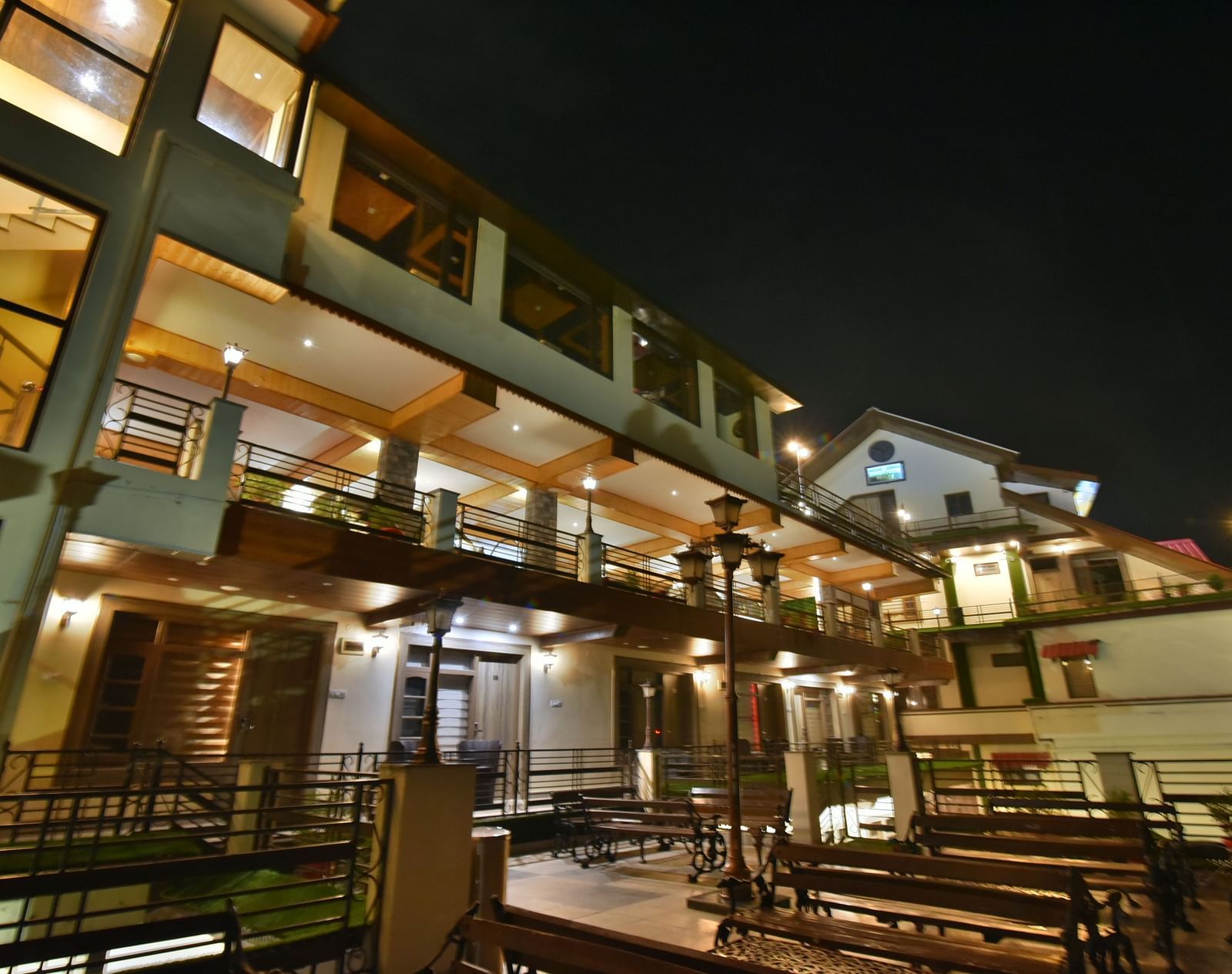 Overview of open terrace at DLS Dalhousie Valley Resort featuring benches and tables during night.