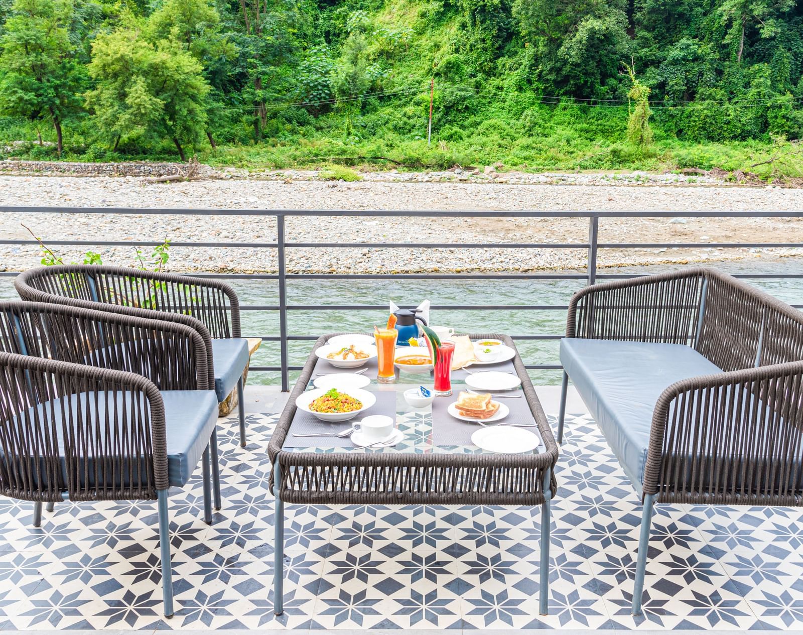 Various dishes plated and kept on the table of a restaurant at DLS Divine River Resort and Spa surrounded by lush greenery and river views.