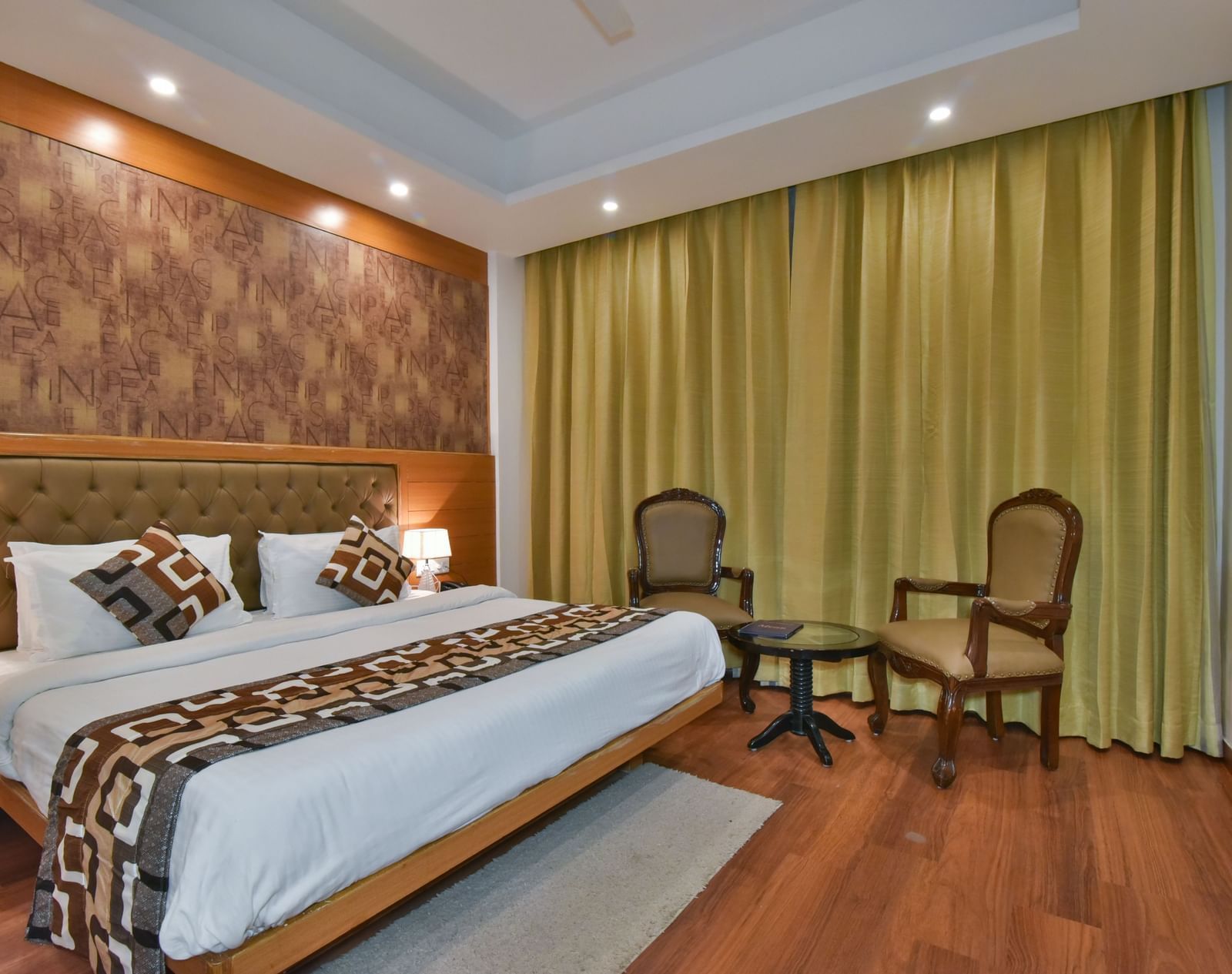 A large bed placed next to two chairs in the Deluxe Room at DLS Highland Resort and Spa, Mussoorie.