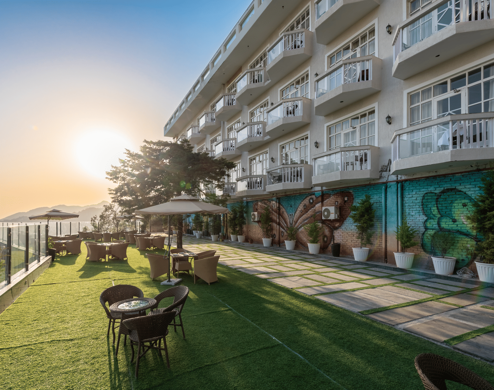 Facade view of DLS Highland Resort and Spa, Mussoorie with comfortable chairs in the lawn at dusk.