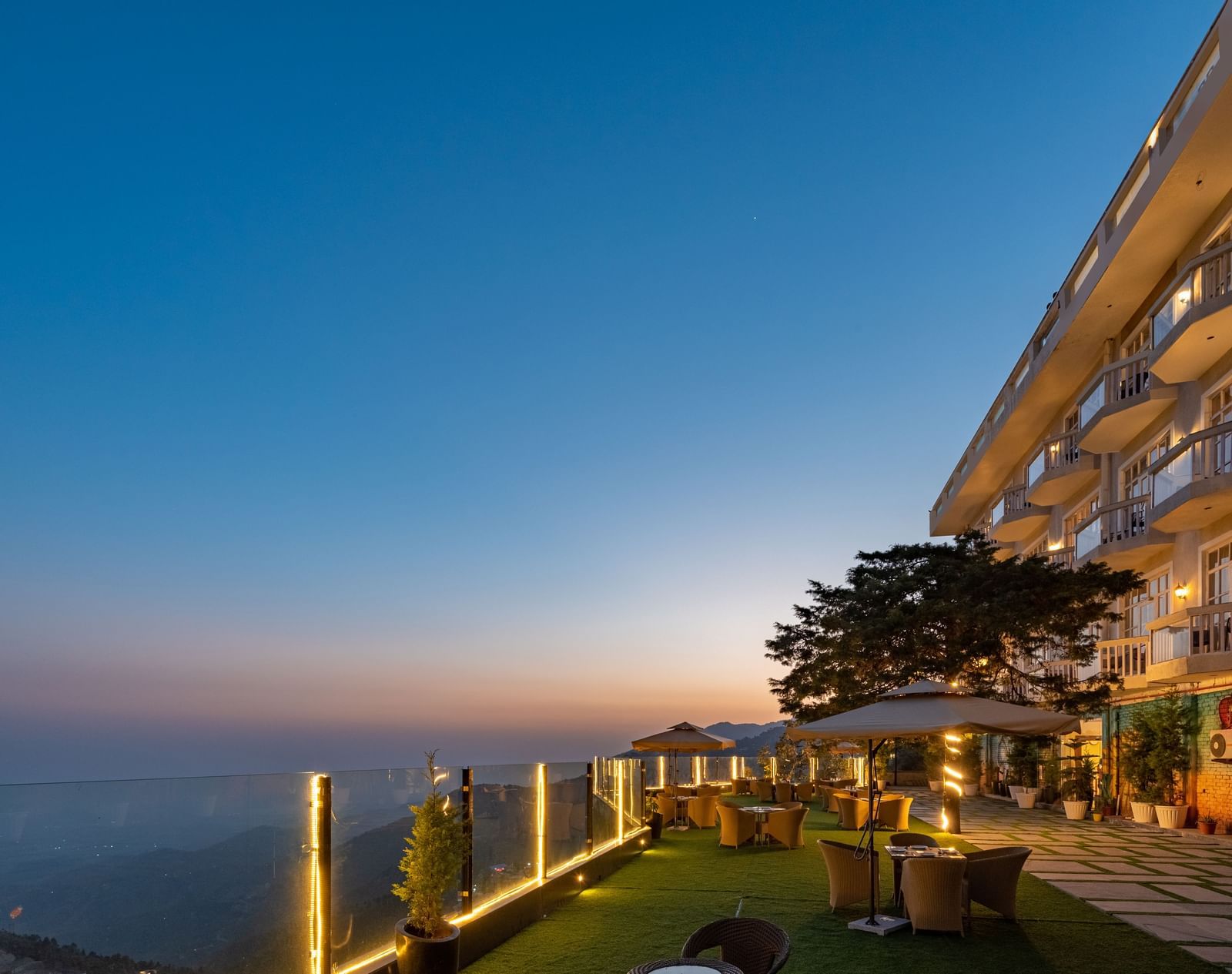 Facade view of DLS Highland Resort and Spa, Mussoorie with comfortable chairs in the lawn at dusk.