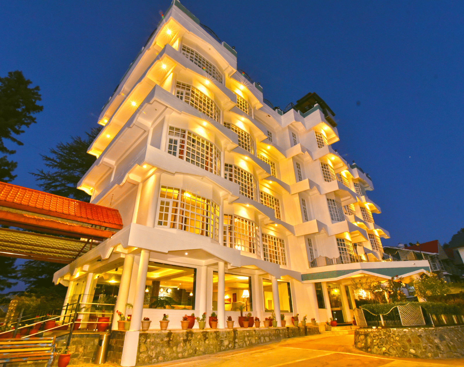 Exterior view of DLS Hillcrest Resort, Shimla, illuminated with warm yellow lights during the evening.