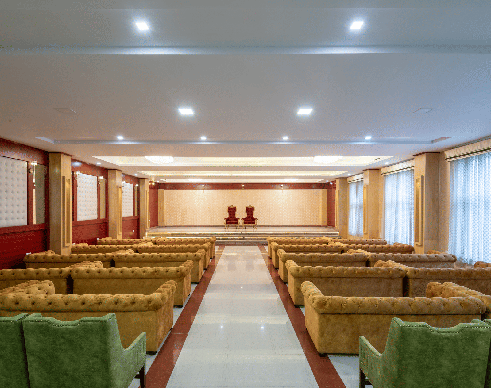 A DLS Hotels banquet hall featuring a combination of sofa and armchair seating facing a stage with 2 ornate chairs.