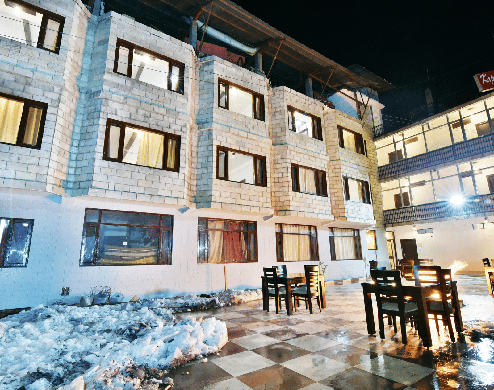 The exterior of DLS Kapoor Resort, Manali, a Hotel in Manali Near Hadimba Temple, at night, showcasing its stone facade, outdoor dining area, and warm lighting.