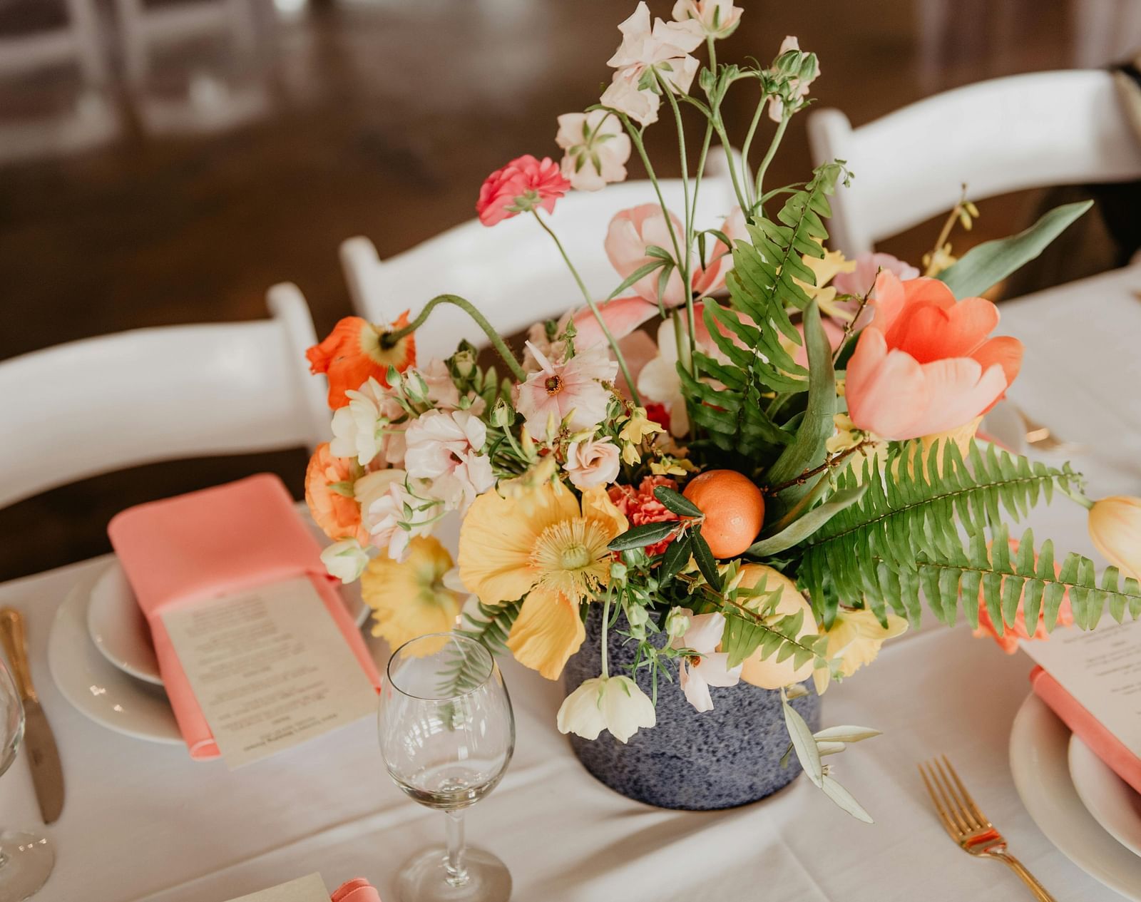A vibrant floral centrepiece featuring an assortment of flowers, sits on a table set for an event.