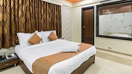 A suite in Krushnai Resort featuring a double bed with yellow runner, a bedside table and a large mirror on the wall.