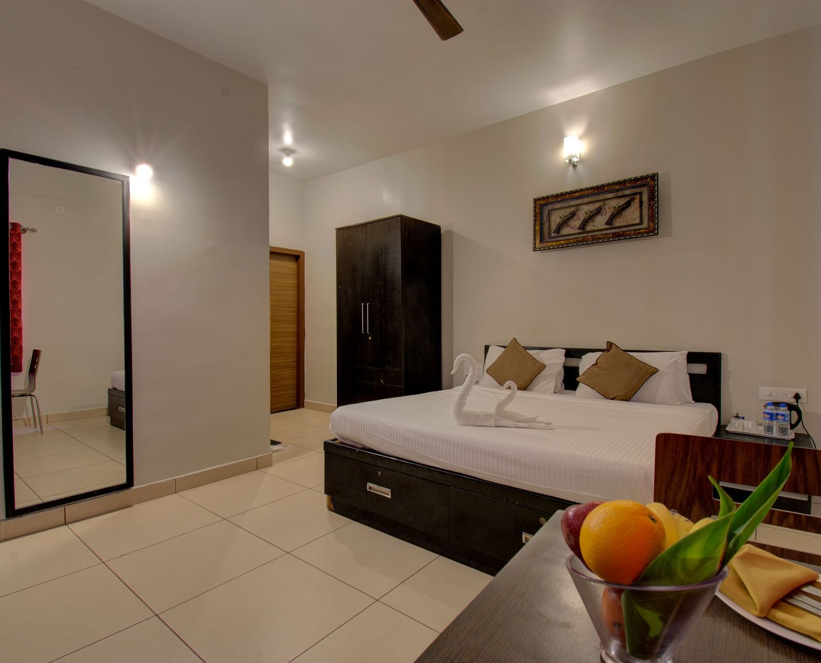 A bedroom with a huge bed, a mirror, Cupboard, a table with fruits on it | Superior Room | Woodstock Resorts, coorg