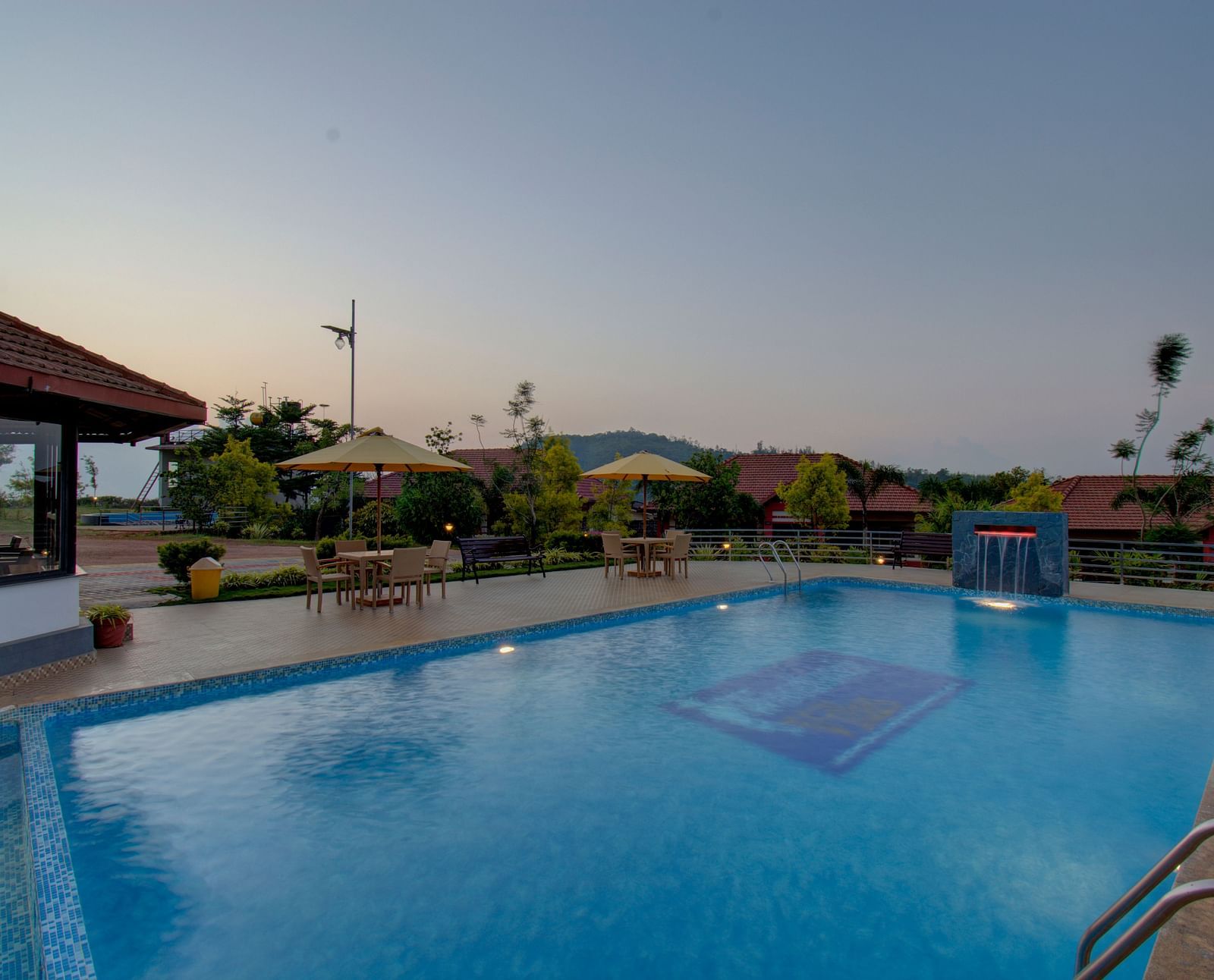 Swimming pool with patios with hills in the background | Woodstock Resorts, Coorg