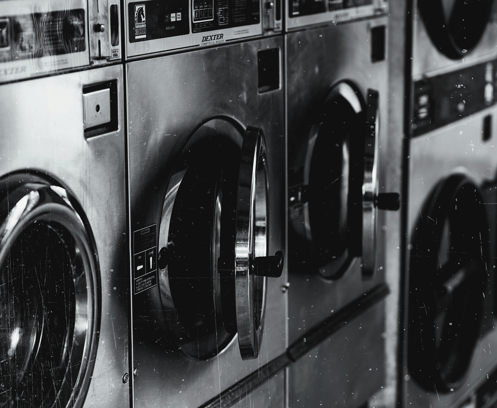 Row of industrial washing machines in a laundromat, black-and-white view.