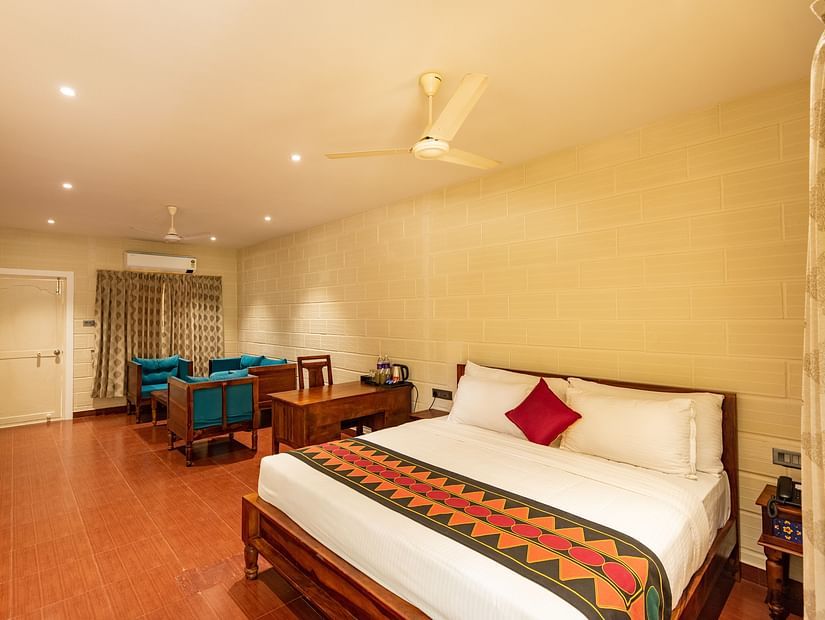 a double bed, sofas and a fan on the ceiling inside the suite at Ibex River Resort, Pollachi
