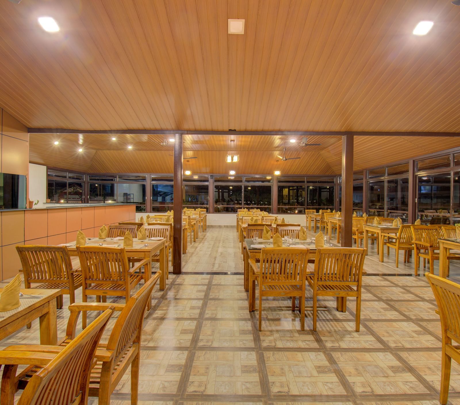 A spacious dining area with wooden tables and chairs, illuminated by warm lighting | Sheesham Restaurant | Woodstock Resorts, Coorg