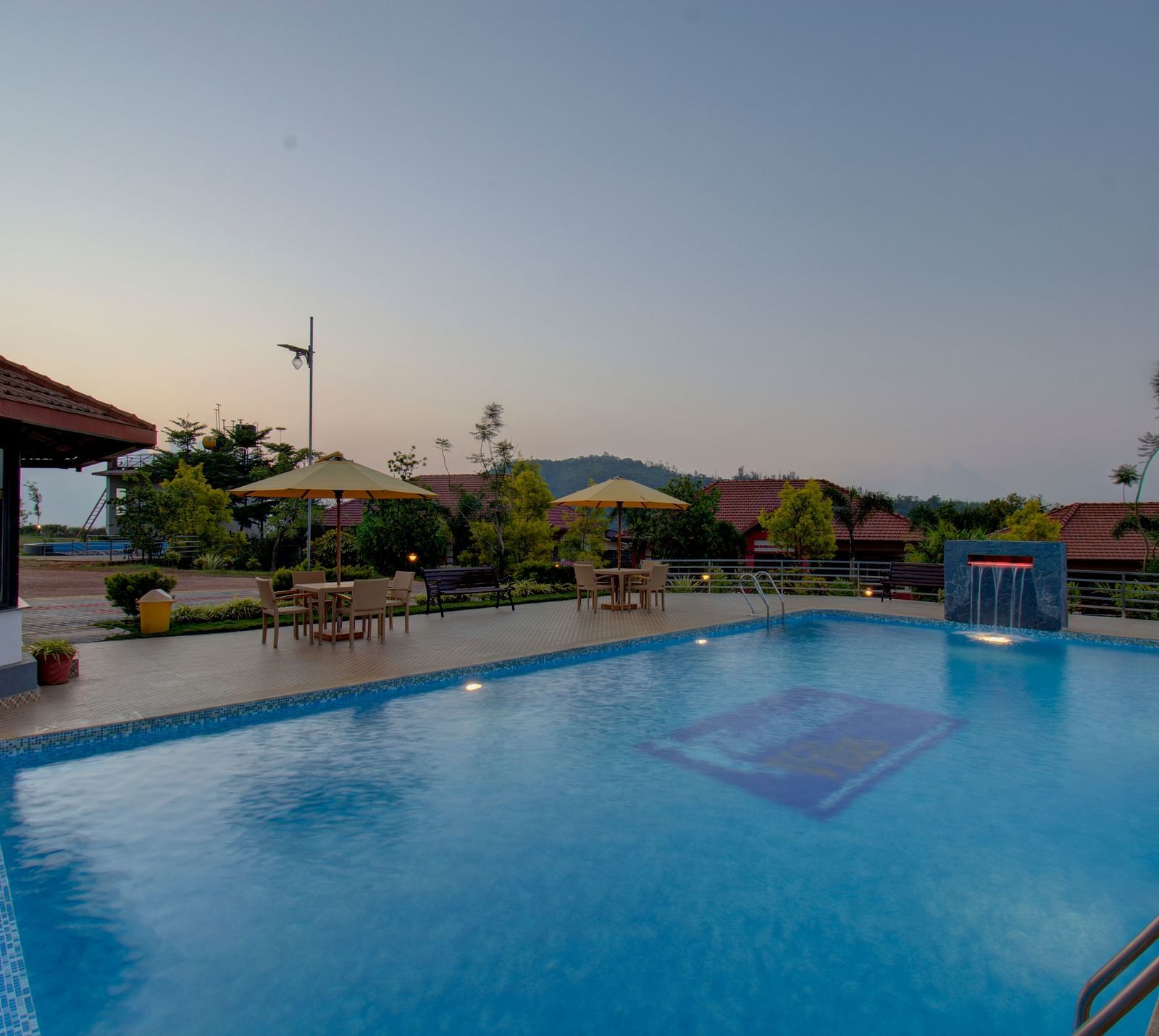 Swimming pool with patios with hills in the background | Woodstock Resorts, Coorg
