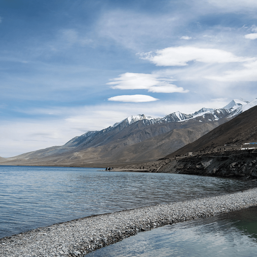 A vast water body surrounded by towering mountains on the sides and in the background.