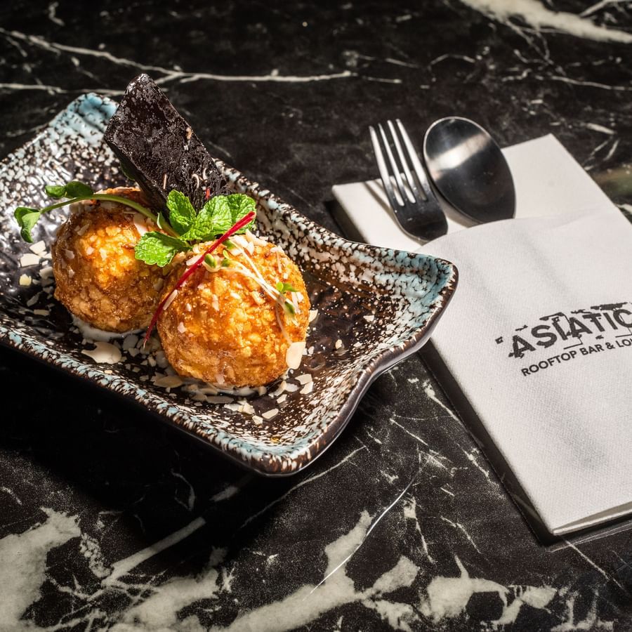 Plate of fried ice cream served at Asiatic Lounge, featuring a crispy golden coating over ice cream scoops, garnished and presented with the lounge’s branded napkin and cutlery on a marble table.