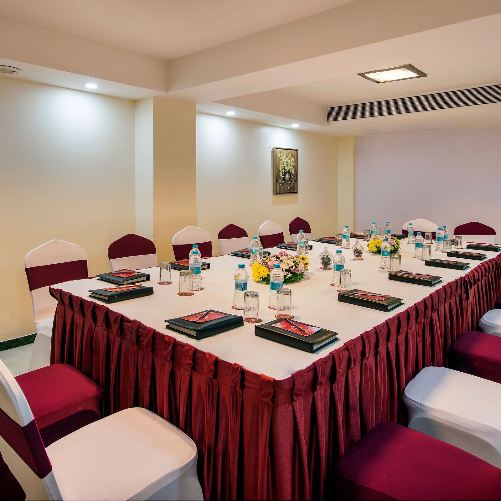 A formal boardroom set up with an elongated table covered in a red patterned cloth, surrounded by chairs at Lords Inn Vadodara.
