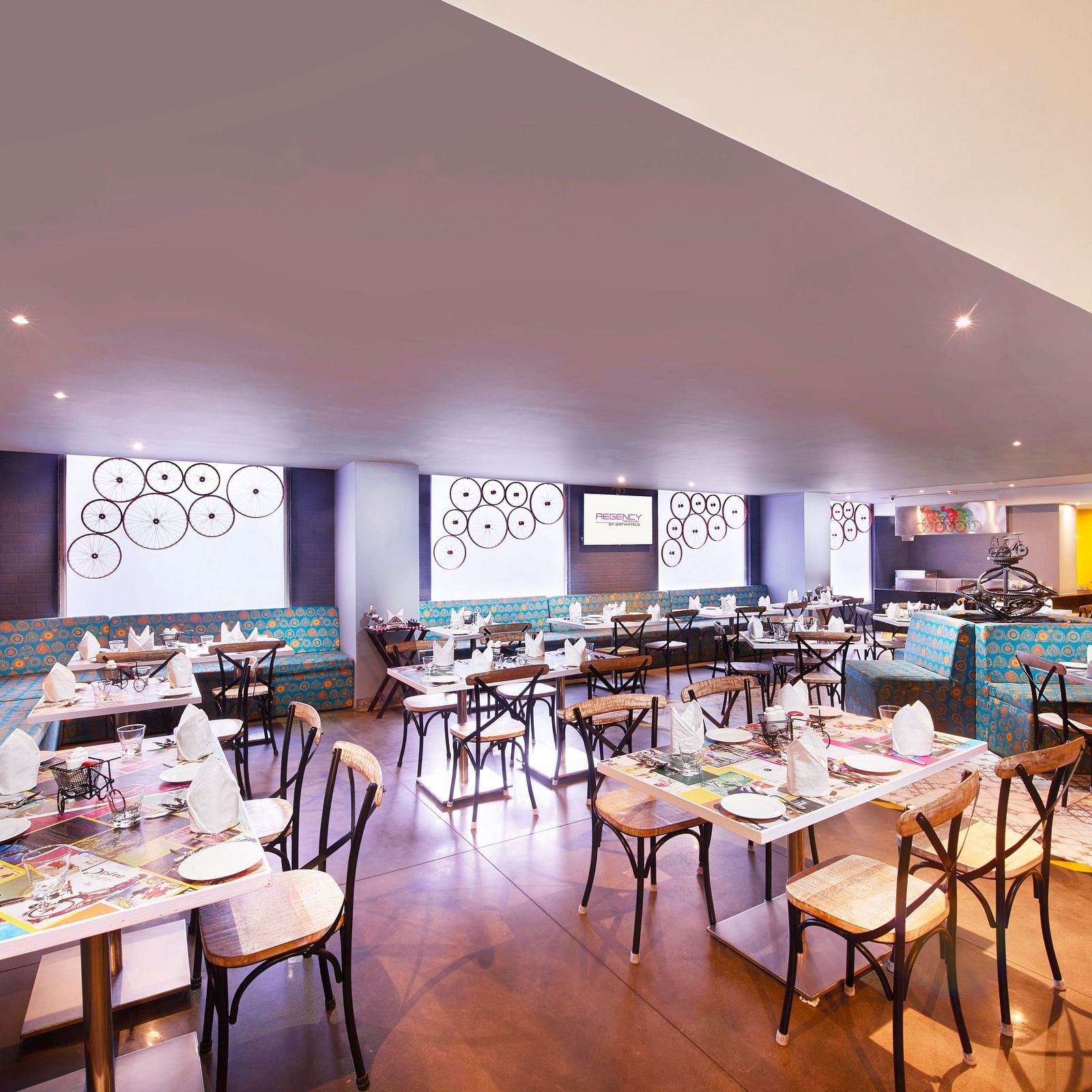 A brightly lit restaurant with chairs, a long bar counter, and a colorful wall mural | Regency Tirunelveli By GRT Hotels