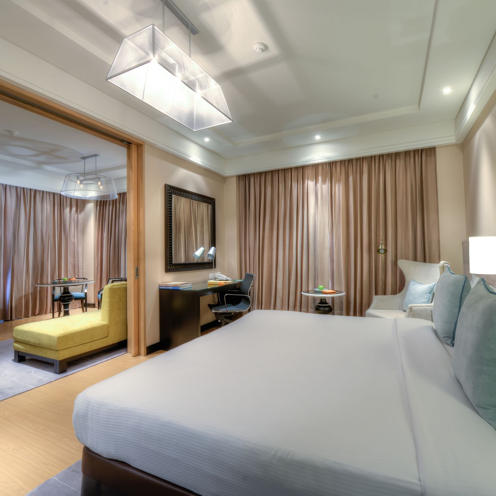 This image shows a spacious hotel room with a large bed, a sitting area, and a TV. The room is decorated in a modern style with neutral colors and plush furnishings.