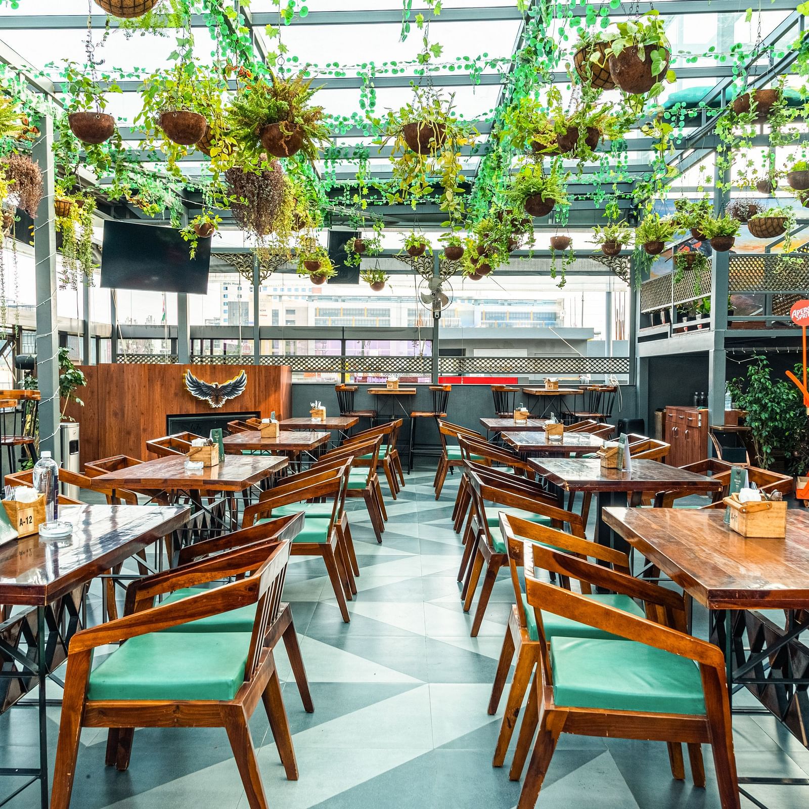 With plants hanging from the roof and wooden chairs with green cushions at Kyba restaurant at Visthara - Urban Boutique Hotel 10
