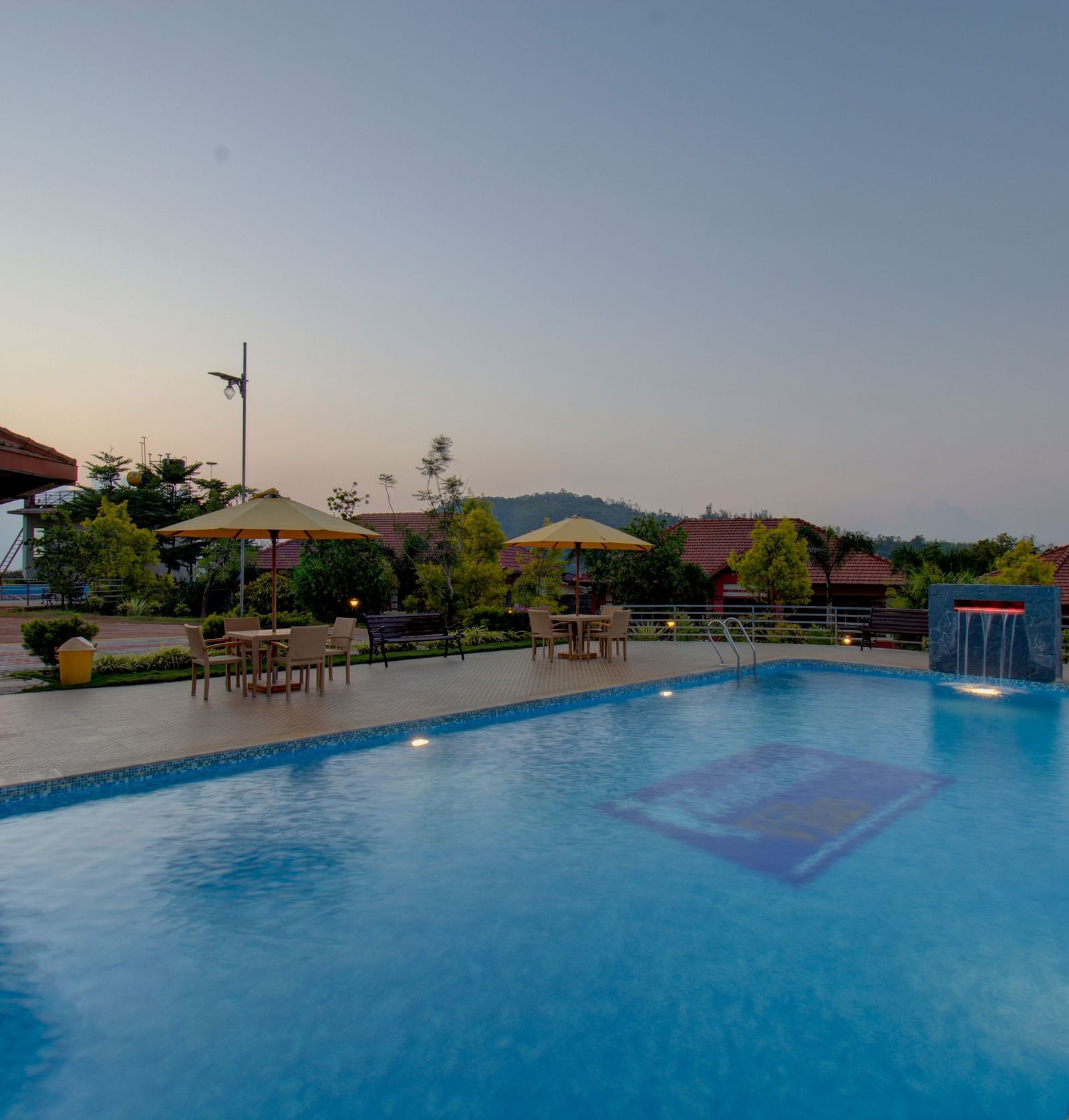 Swimming pool with patios with hills in the background | Woodstock Resorts, Coorg