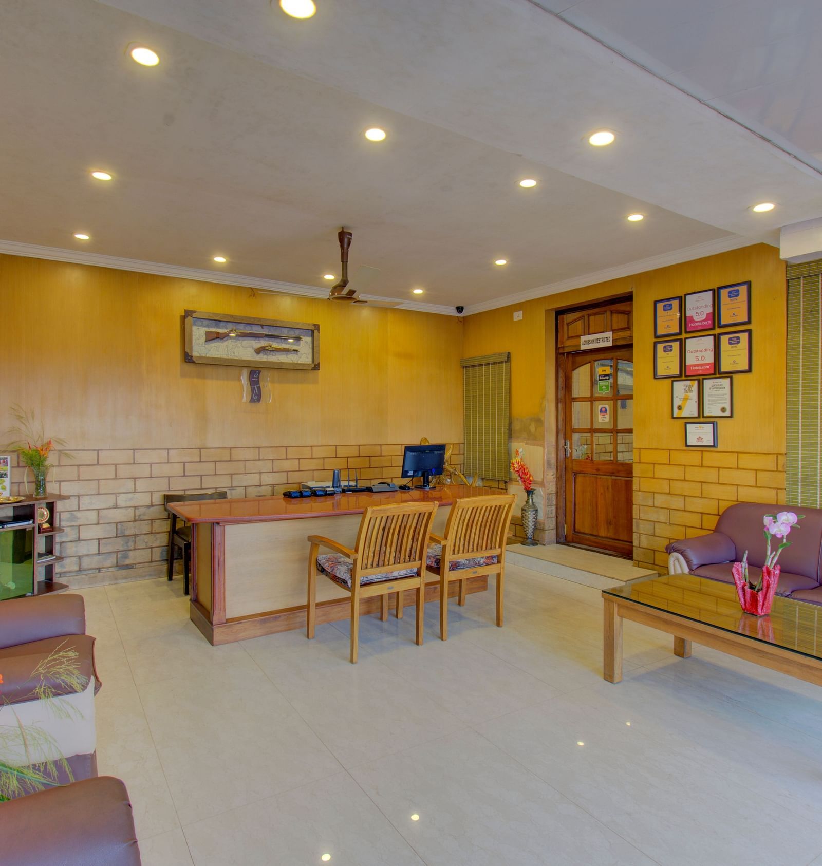 A cosy reception area with a brown sofa, wooden furniture, and warm lighting | Woodstock Resorts, Coorg
