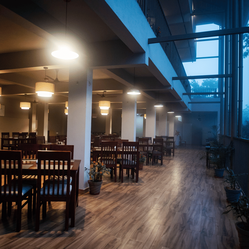 A restaurant interior featuring wooden tables and chairs with pendant lights, overlooking the forest - Abad Brookside Lakkidi, Wayanad