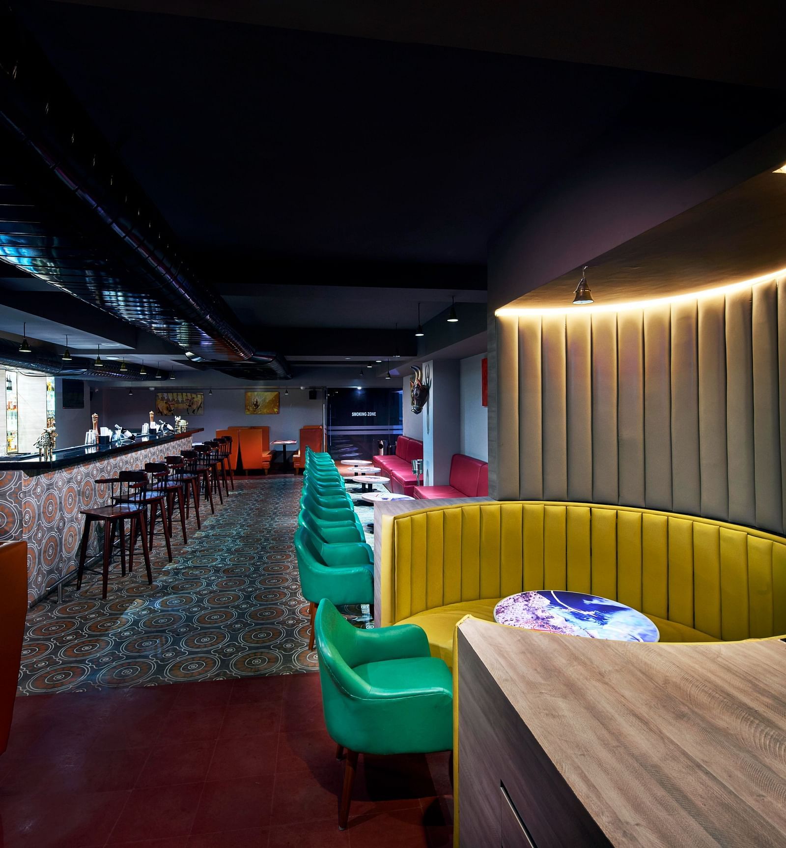 A brightly lit bar with red couches, a long bar counter, and a colorful wall mural | Regency Tirunelveli By GRT Hotels