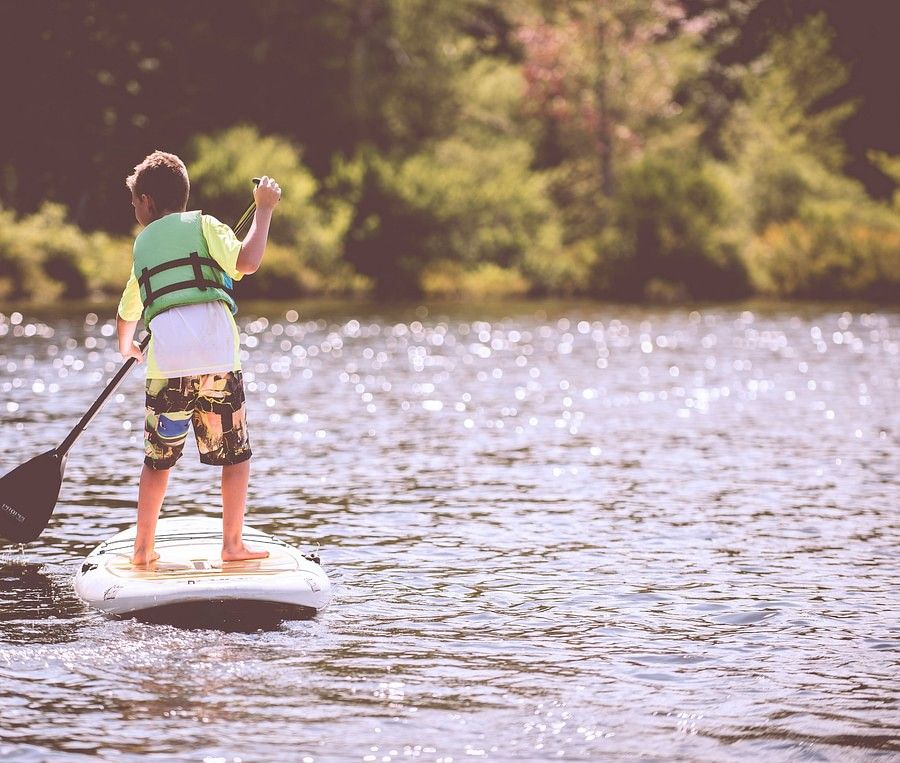 alt-text The image shows a boy paddle boarding on a lake.