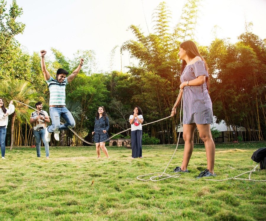 A group of adults and children playing tug of war in a grassy outdoor area, displaying joy and family bonding during a playful and competitive moment.