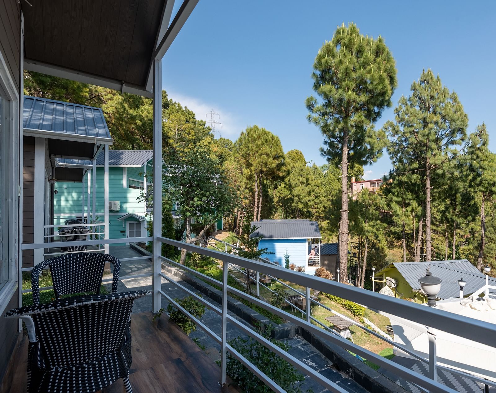 Balcony with two chairs overlooking trees and buildings under a blue sky - DLS Nature Trinket Resort, Dalhousie.
