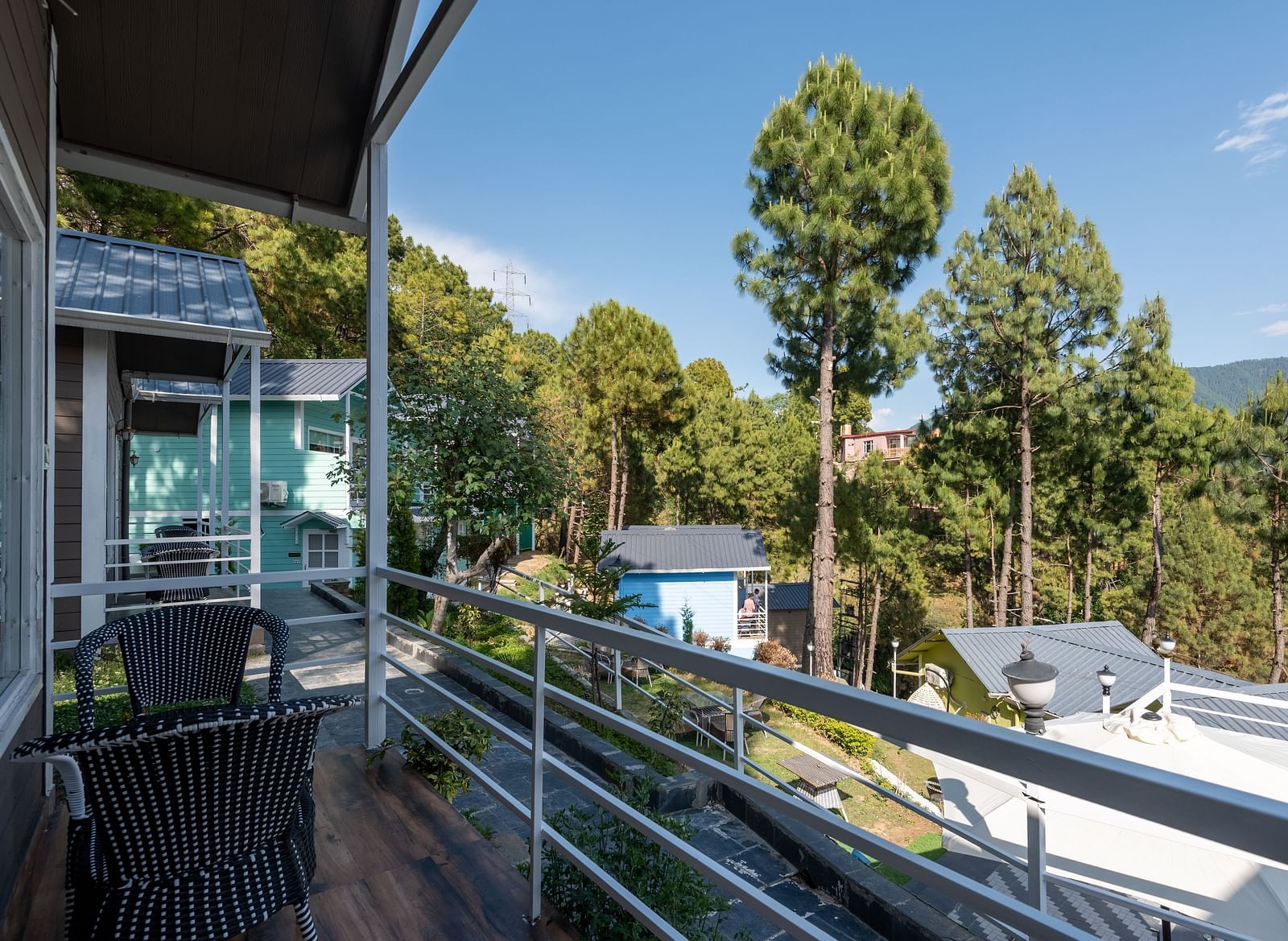Balcony with two chairs overlooking trees and buildings under a blue sky - DLS Nature Trinket Resort, Dalhousie.