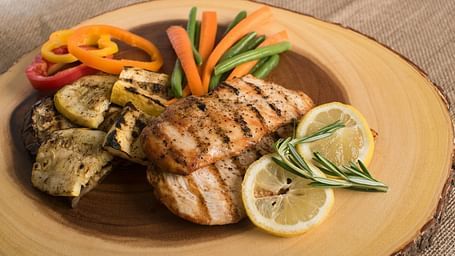 Fried meat and vegetables like carrot, beans, capsicum, and corny garnished with melted butter, and lemon placed in a plate on a wooden log