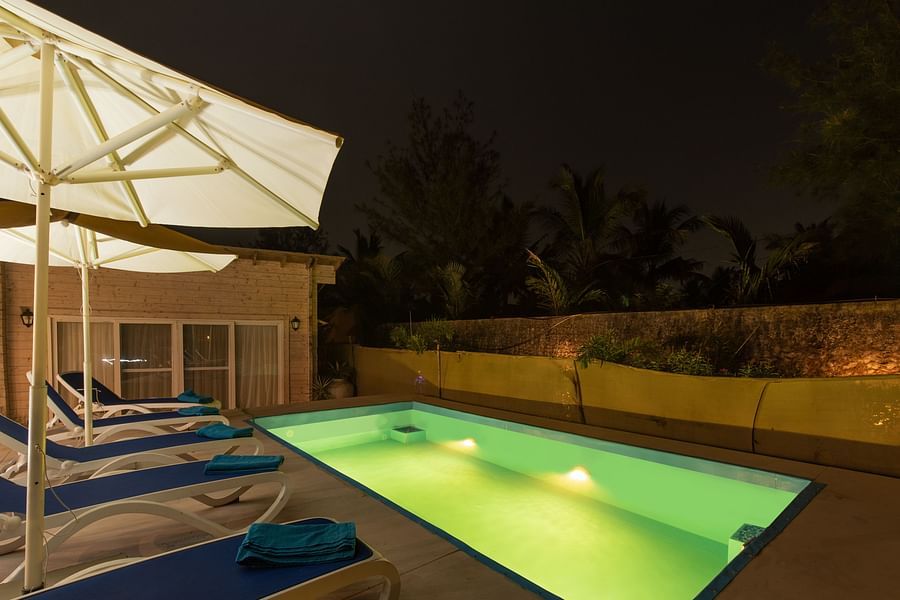 Swimming poolside view at night with pool loungers umbrellas and lightings