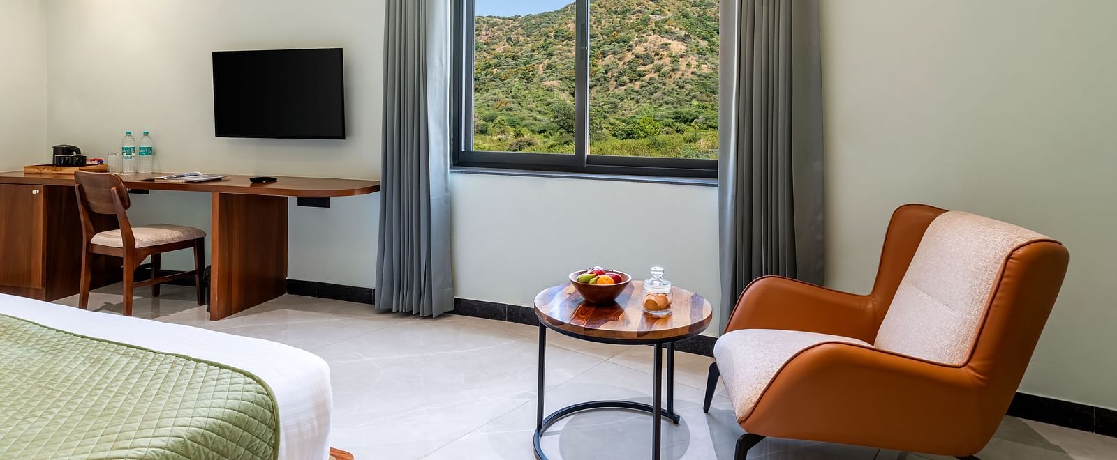 Valley View Room with a king size bed, seating area by the window, and a desk with a television at The Qualia Resort Club & Brewery, Udaipur.