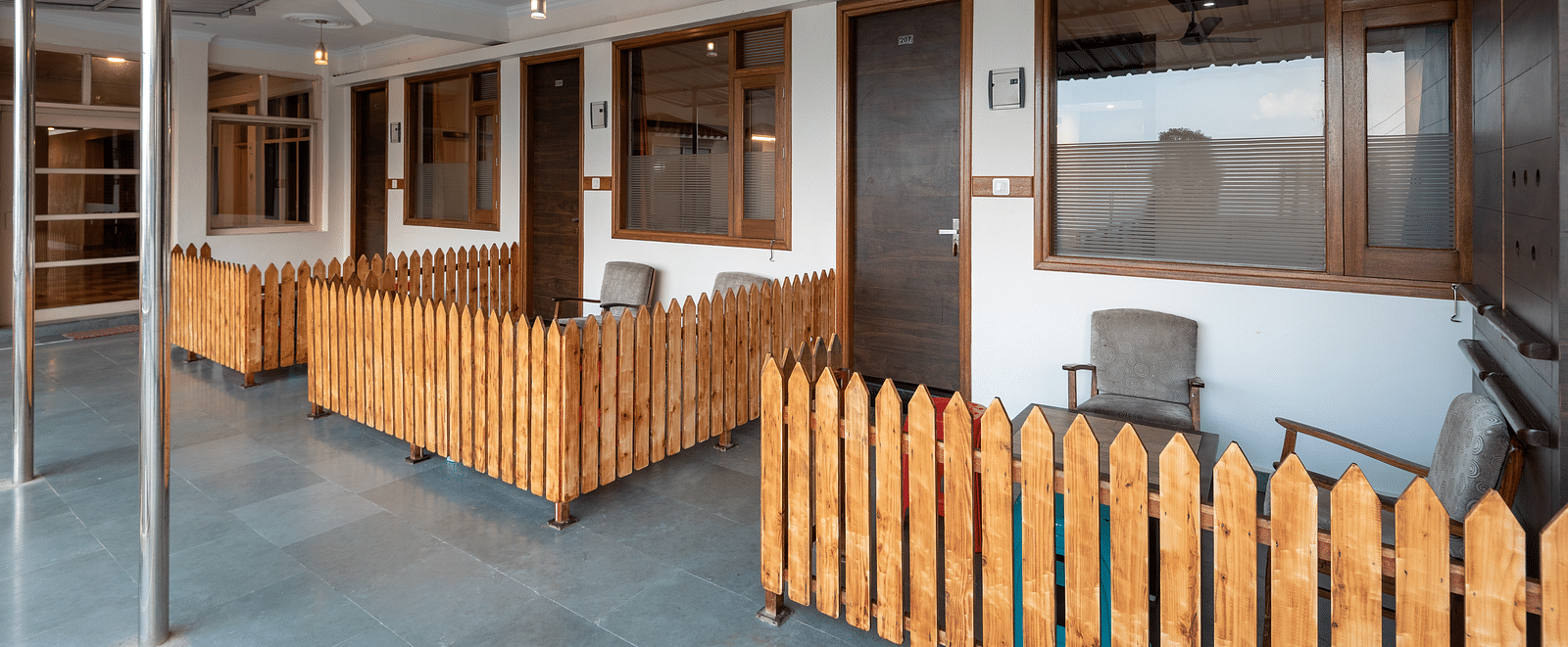 Common balcony with wooden fencing and chairs in front of room doors - DLS Meghavan Resort, Dharamshala