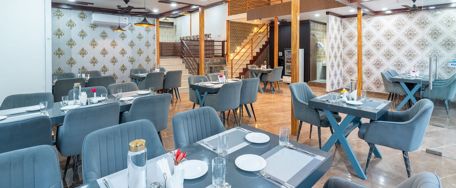 Stylish restaurant interior with neatly arranged tables, gray upholstered chairs, ceiling fans, and patterned accent walls - DLS Nature Trinket Resort, Dalhousie.