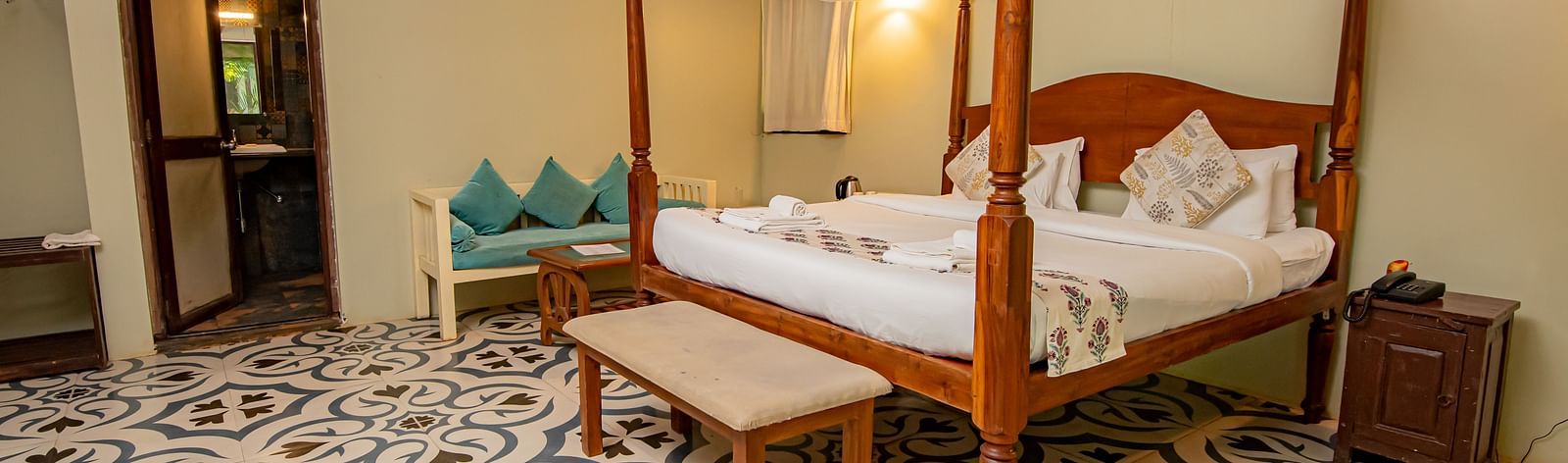 Four-poster canopy bed in a well-lit room with patterned flooring and wooden ceiling beams at De Soul Santé, Morjim.
