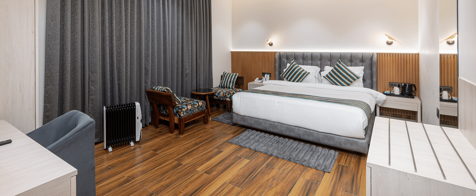 The deluxe room with a bed, chairs, coffee table, and a full length mirror - DLS The Emerald, Nainital