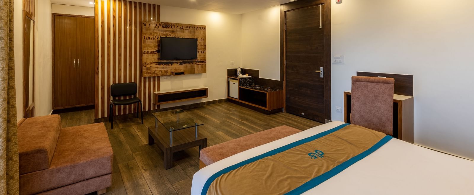 Premium room with modern wooden decor, TV, mini fridge, and a seating area - DLS Meghavan Resort, Dharamshala