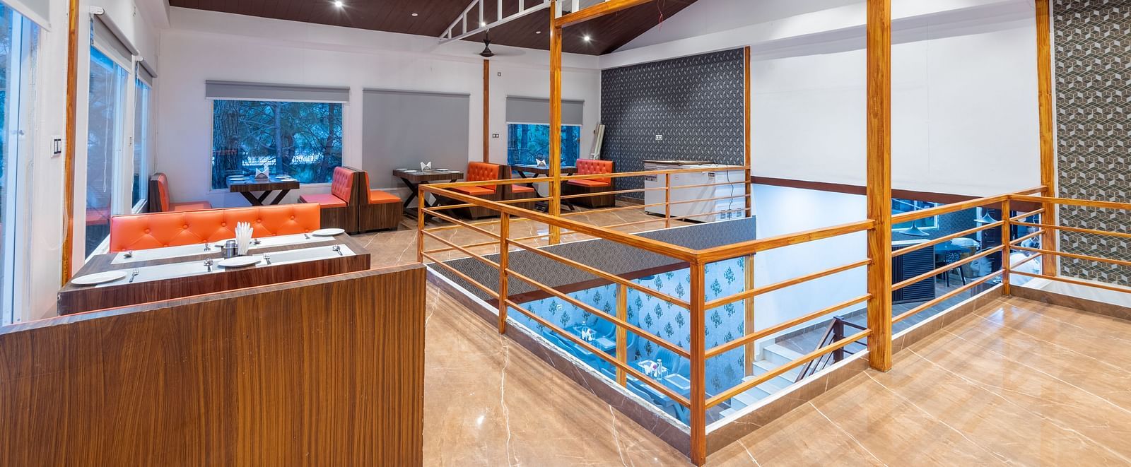 Spacious restaurant interior with orange booth seating, wooden railings, tiled floor, and large windows - DLS Nature Trinket Resort, Dalhousie.