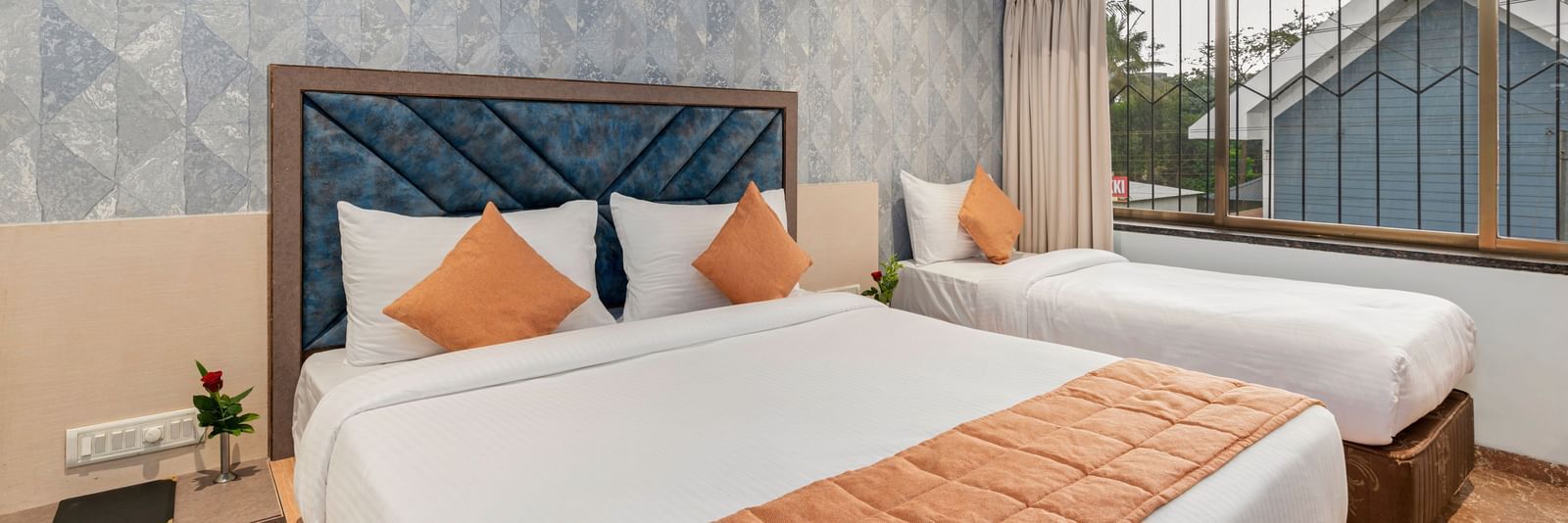 Double bed and a single bed setup at Emerald Retreat, Tungarli with a soft blue accent wall, large windows, and ample natural light.