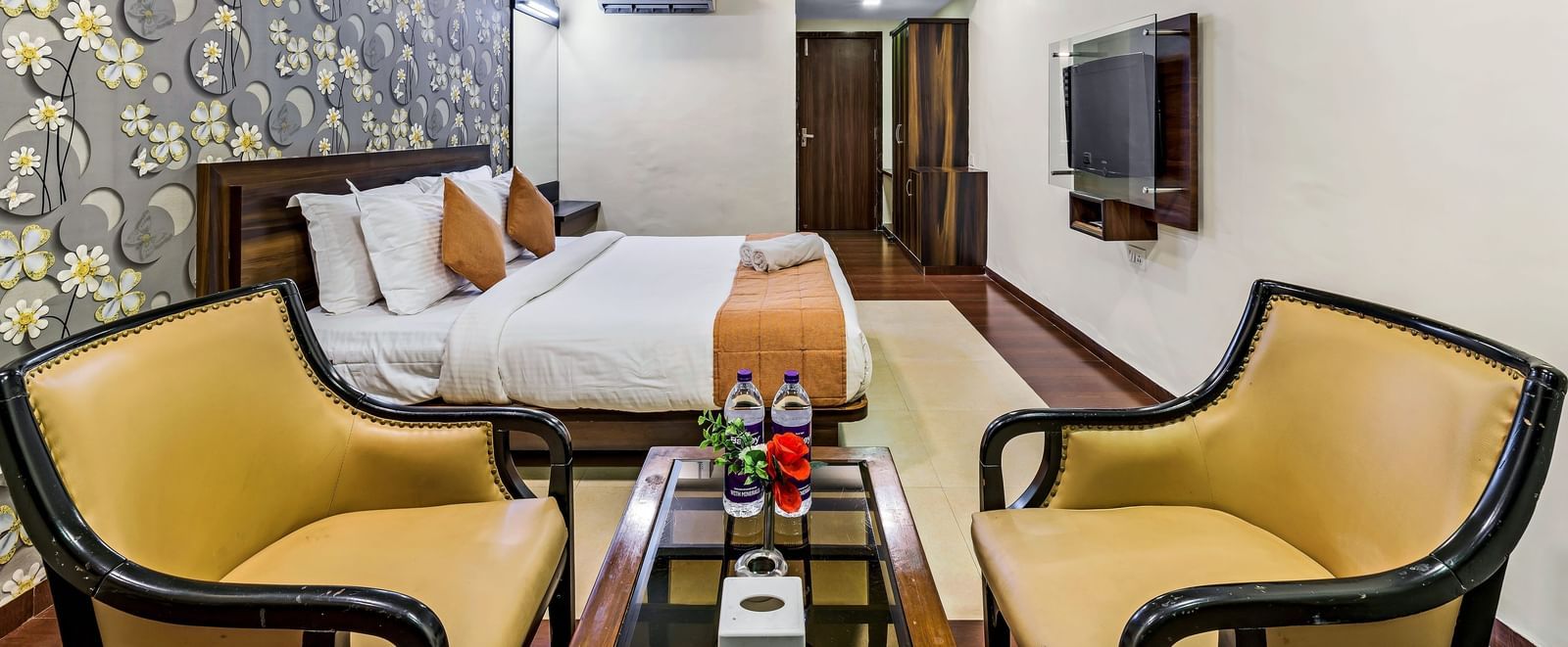 A royal executive room in Krushnai Resort featuring a double bed with yellow runner and two lounge chairs.