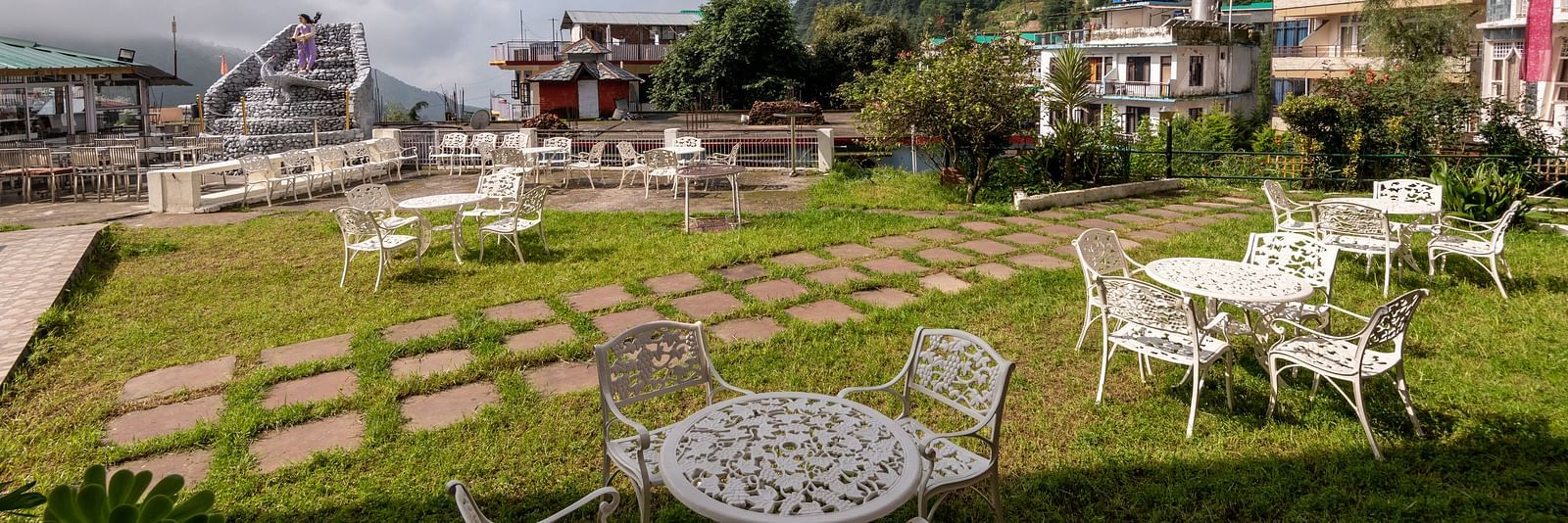 Outdoor seating area with tables and chairs on a lawn overlooking a mountain view - DLS Meghavan Resort