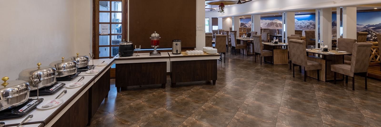 A dining room with tables and chairs, a buffet line, and a ceiling fan - DLS Meghavan Resort