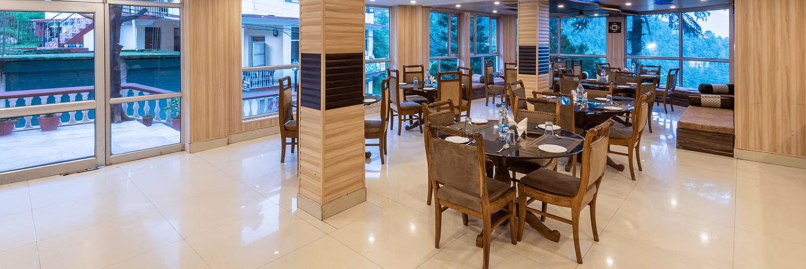 A wide angle shot of a dining area inside the resort featuring tables and chairs | DLS Anupam Resort, Dharamshala