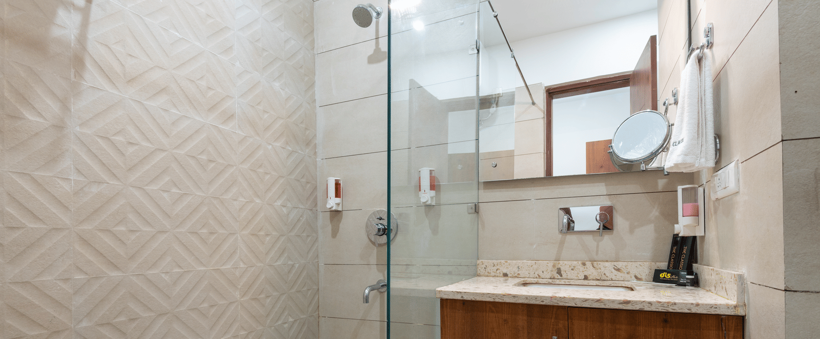 Deluxe bathroom featuring a mirror above a washbasin with a wooden cabinet below and a spacious shower area at DLS The Classio