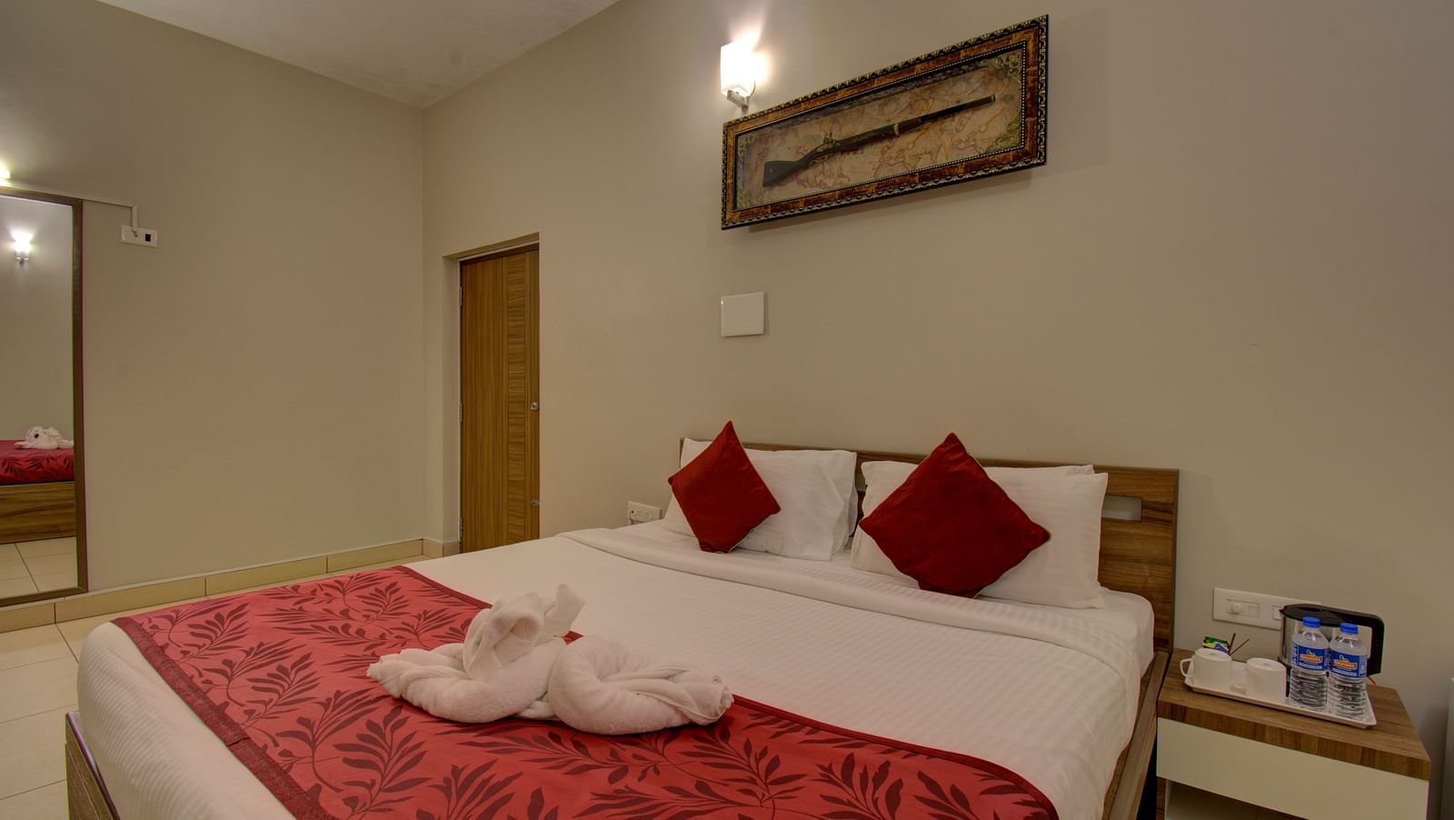 A swan made with of towel on a huge bed, a side table, mirror, wooden door and an wall art | Superior Room | Woodstock Resorts, Coorg