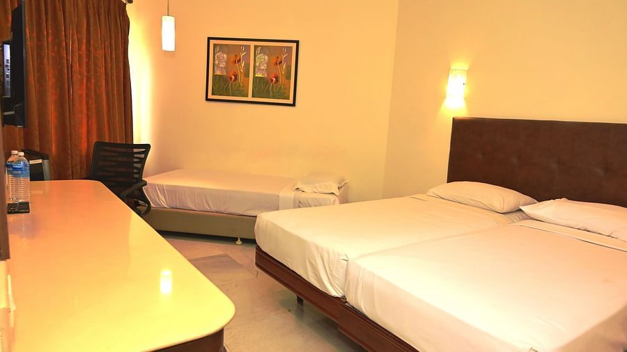 Suite with plush double-occupancy bedding under warm lighting and wall hangings near the window draped with curtains at Jayaram Hotel, Pondicherry